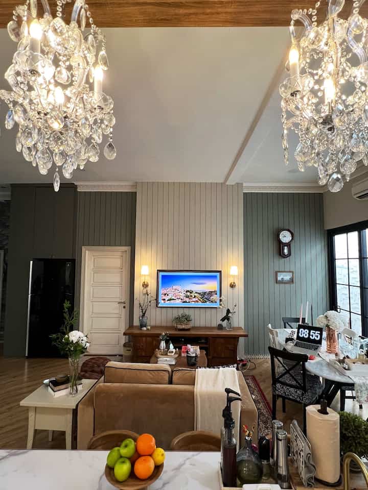 White and brown toned dining and living room featuring crystal chandeliers and marble dining table in a French Country style space