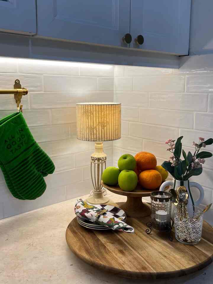 Cozy kitchen corner with white tile backsplash and natural wood round trays, featuring fruits and decorative tableware