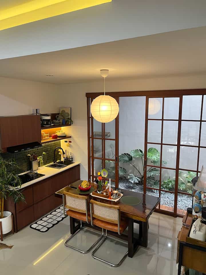 Compact dining room and kitchen with wood tones and green accents, featuring a large round pendant light creating a cozy atmosphere