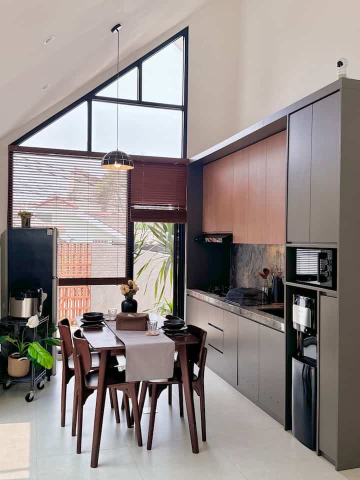Modern kitchen and dining room with high ceiling and large windows, featuring brown wooden furniture and gray cabinets for a warm, modern atmosphere