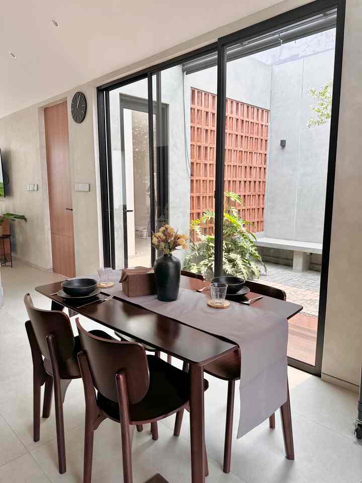 Brown furniture in a white-toned dining room featuring a dining table, chairs, tableware, and plants creating a natural ambiance