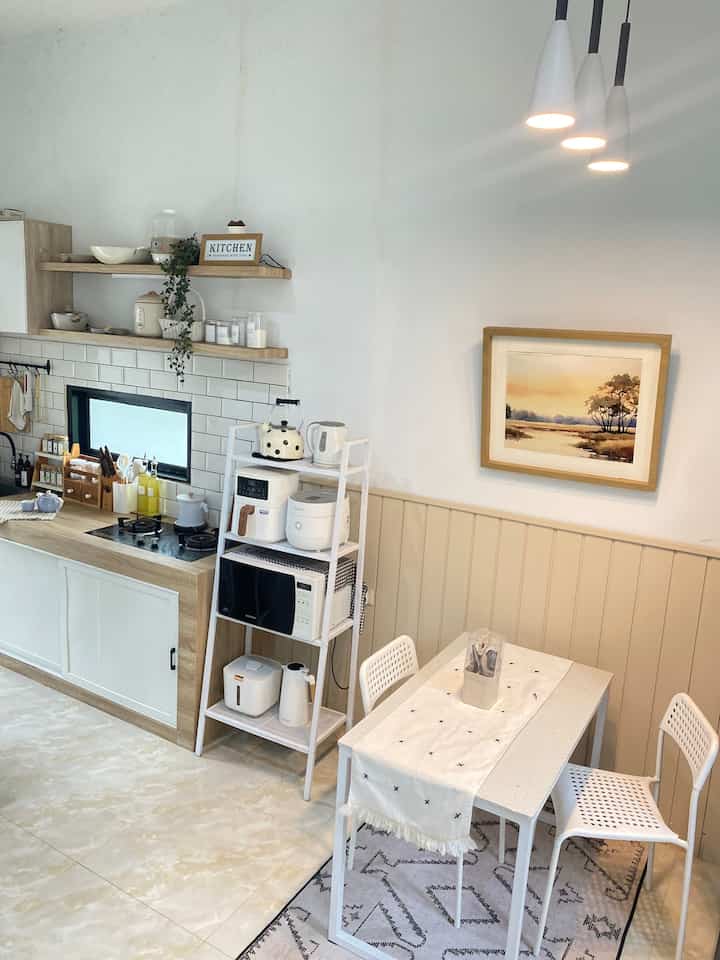 White and beige toned kitchen space featuring modern minimalist dining table and appliance shelving with clean design
