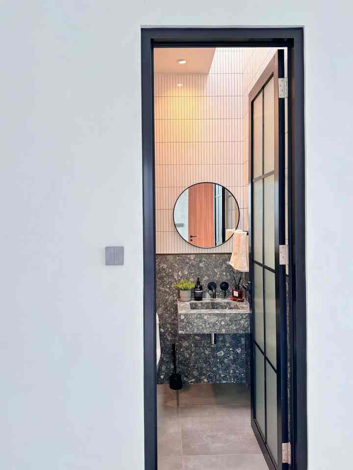 Small modern restroom with gray tiled floor and black door frame, featuring a marble washbasin and round mirror inside