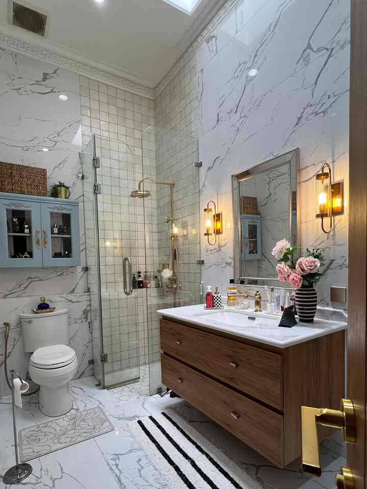 White and wood tone bathroom featuring gold accessories and vintage wall sconces creating a luxurious atmosphere