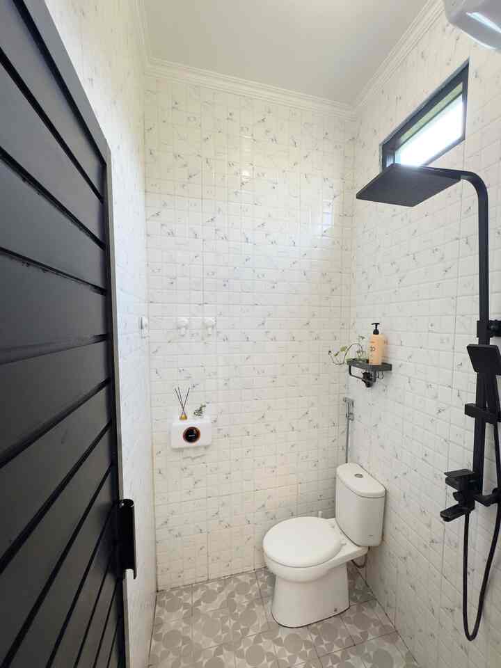 Compact bathroom with white tiled walls and floor, featuring a black shower column and toilet in a clean modern design