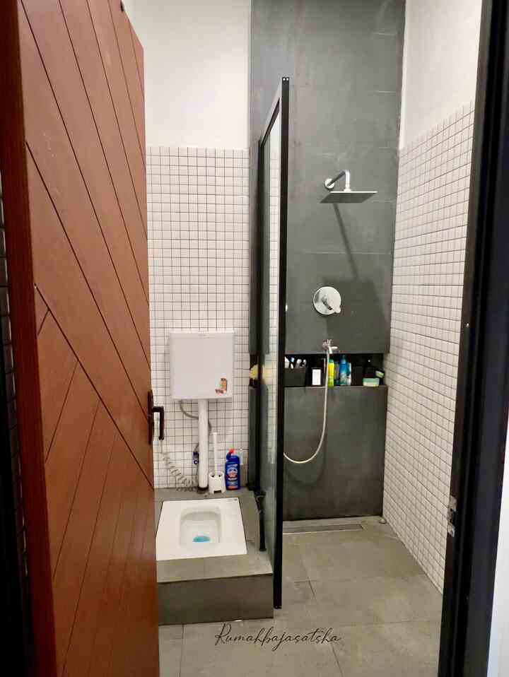Rumah ini dilengkapi dengan kamar mandi di lantai 1 dan lantai 2, dengan desain dan fungsi yang menyesuaikan kebutuhan penghuni:
1.	Kamar Mandi Lantai 1
	• Fasilitas: Menggunakan WC duduk berwarna putih dengan aksen sanitary chrome untuk kesan modern. Dilengkapi wastafel di dekat pintu untuk memudahkan mencuci tangan sebelum masuk rumah, serta kabinet berbahan kayu sebagai tempat penyimpanan stok sabun.
	•	Dimensi: Berukuran 1x3 meter, memberikan ruang yang cukup untuk kenyamanan.
	•	Material: Lantai dan sebagian dinding dilapisi granite abu untuk tampilan elegan, sementara sebagian dinding menggunakan keramik mozaik sebagai aksen, dan sisanya dicat untuk kesan bersih dan minimalis.
	•	Ventilasi: Menggunakan exhaus fan & ventilasi udara alami untuk menjaga kelembapan ruangan.

2.	Kamar Mandi Lantai 2
	•	Fasilitas: Menggunakan WC jongkok berwarna putih dengan sanitary chrome, serta dilengkapi shower set dengan kran bercabang, mempermudah tamu yang ingin berwudhu.
	•	Dimensi: Berukuran lebih luas, yaitu 1.5x3 meter.
	•	Material: Sama seperti lantai 1, menggunakan kombinasi granite abu, keramik mozaik, dan cat dinding.
	•	Sirkulasi Udara: Memanfaatkan exhaust fan untuk menjaga udara tetap segar dan tidak lembap.

Desain kamar mandi ini memadukan fungsi dan estetika, menciptakan ruang yang nyaman dan praktis untuk penghuni maupun tamu.
#KeramikKamarMandi 
#PintuKamarMandi #CatKamarMandi #WarnaKamarMandi 
#DindingKamarMandi #KeramikDinding #KeramikLantai
#KamarMandiMinimalis
#InspirasiKamarMandi