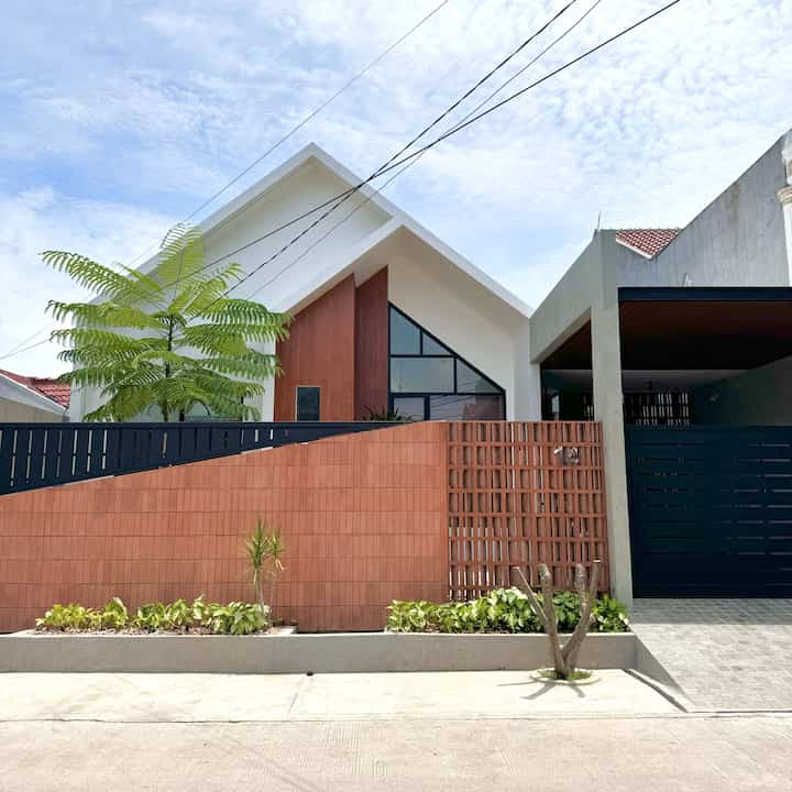 Tema fasad di rumah aalo ini Kontemporer dengan menggabungkan konsep scandi, minimalis, tropical dan sedikit sentuhan industrial dibagian carport yang memberikan kesan modern. 

Kami memilih gaya ini karena ingin menciptakan suasana yang hangat, sekaligus mencerminkan gaya hidup yang dinamis. Fasad kontemporer juga memungkinkan penggunaan elemen desain yang inovatif, yang sangat cocok dengan lingkungan sekitar.

Untuk mencapai style ini, kami memilih material seperti panel kayu alami, besi, roster, kaca besar dan kami tambahkan tanaman. Kombinasi material ini tidak hanya memberikan tampilan yang estetis, tetapi juga memastikan pencahayaan alami yang baik di dalam rumah. Membuat rumah terasa lebih terang dan terbuka 🥰

#pagarrumah #pagarrumahminimalis #warnacatpagar #plavonPVC #catrumah #rumahscandinavian #rumahindustrial #rumahminimalis #InspirasiFasad #StyleFasad 