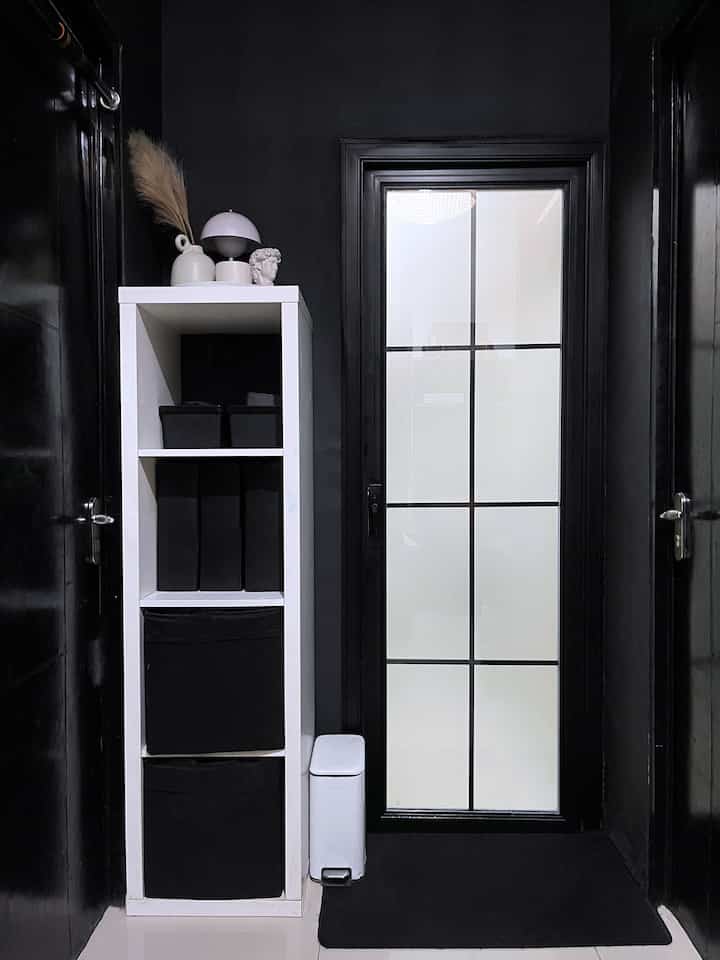 Modern entrance with black walls and doors, featuring a white storage cabinet and trash bin neatly arranged