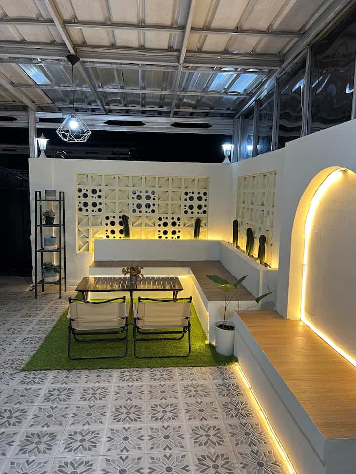 White and wood tone veranda featuring greenery and LED lighting, creating a cozy semi-outdoor lounge atmosphere