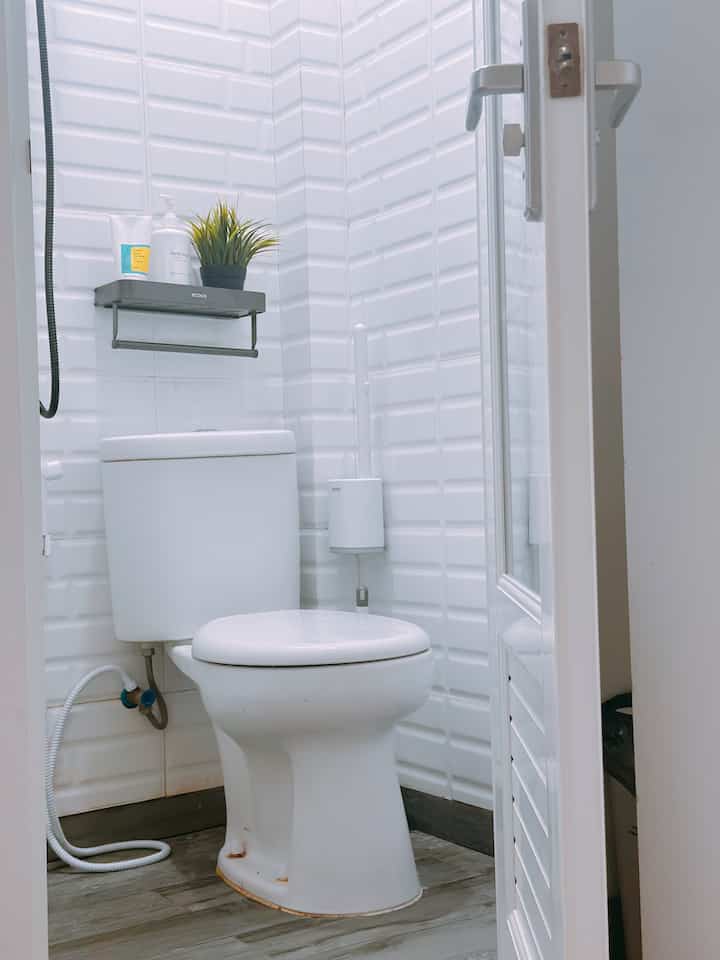 Small bathroom with white brick-pattern tiles and wood-toned floor, featuring toilet and towel rack in a clean layout
