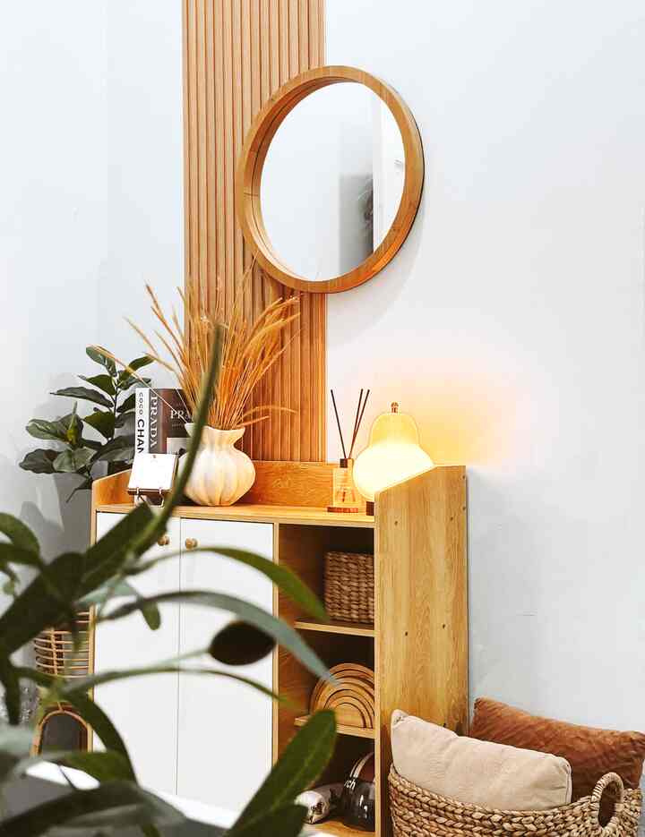 Minimal style entrance with white walls and wood tones featuring round mirror, wooden storage cabinet, and plants