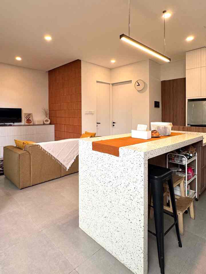 A modern living room and kitchen blending warm brown tones with white background, featuring a kitchen island with a table runner as focal point