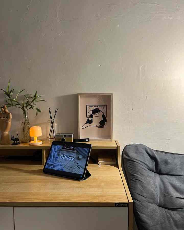 Natural wood and gray toned home office space featuring table lamp and cat illustration framed art with cozy atmosphere