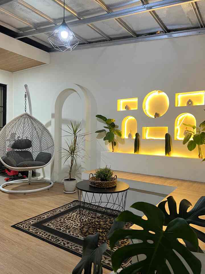 Modern entrance space with natural wood-tone flooring and plants, featuring black furniture and pendant lighting creating a cozy atmosphere