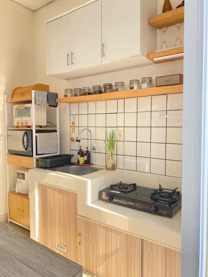 A modern kitchen in white and brown tones featuring a stove, sink, plants, and wine glasses with a cozy atmosphere