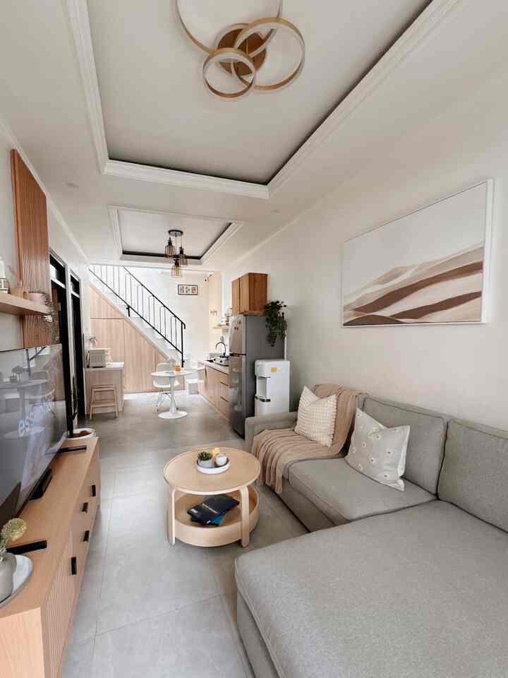 White and wood tone studio apartment open plan living room and kitchen featuring gray sectional sofa and round coffee table in a minimal space