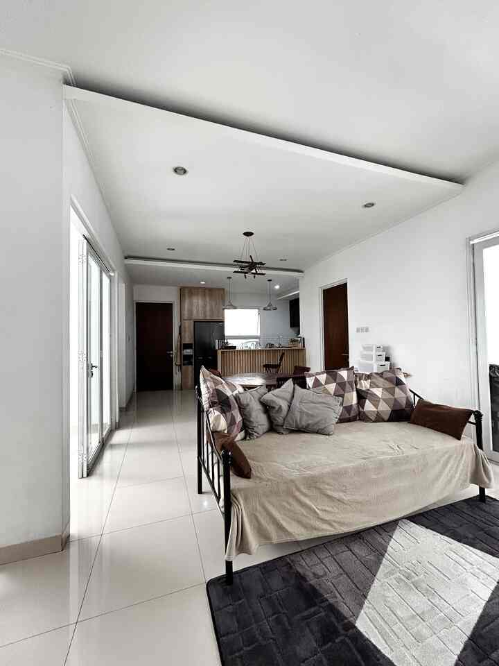 Modern living room and kitchen space in white and brown tones, featuring beige sofa with multiple cushions