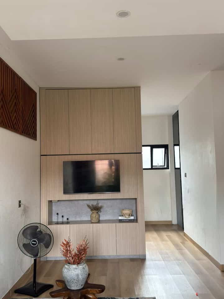 Di rumahku, ruang tamu menyatu dengan mini pantry dengan total ukuran 3x9 meter. Konsep open space seperti ini membuat rumah terasa lebih luas, lapang, dan nyaman, terutama untuk berkumpul bersama keluarga. Namun, agar ruangan tetap terlihat rapi dan tertata, aku menyiasatinya dengan beberapa langkah berikut:
	1.	Menggunakan karpet sebagai pembatas visual
Meletakkan karpet bermotif sederhana di area ruang keluarga untuk menciptakan pembatas visual antara ruang keluarga dan pantry. Selain berfungsi sebagai dekorasi, karpet ini juga memberikan kesan hangat dan nyaman pada ruangan.
	2.	Memilih furnitur multifungsi
Sofa berbentuk L menjadi pilihan utama. Selain memberikan kesan modern, sofa ini memiliki ruang penyimpanan tersembunyi di bawahnya, yang sangat berguna untuk menyimpan barang-barang seperti bantal tambahan atau mainan anak-anak.
	3.	Kabinet gantung minimalis dengan motif kayu
Di pantry, saya menggunakan kabinet gantung bermotif kayu untuk menyelaraskan dengan tema rumah. Kabinet ini tidak hanya mempercantik ruangan, tetapi juga membuat area pantry lebih rapi dengan menyembunyikan peralatan dapur di dalamnya.
	4.	Dekorasi yang fungsional
Dengan menambahkan toples-toples kaca untuk menyimpan teh / kopi di pantry. Selain fungsional, toples ini juga menjadi elemen dekoratif yang menarik. Di ruang keluarga, aku menambahkan beberapa tanaman hias kecil untuk menambah kesan segar dan alami.

Dengan perpaduan furnitur yang tepat, dekorasi sederhana, dan penataan yang efisien, ruang tamu dan pantry di rumah tetap terasa rapi, nyaman, dan fungsional meskipun keduanya berada dalam satu area open space. Rumah sederhana tetap bisa terlihat indah dan tertata dengan baik.

#KitchenSet #SofaMinimalis #sofainforma #sofabed
#KitchenSetMinimalis #PlavonPVC 
#WarnaCatRumah #catputih #WallpaperDinding 
#WallpaperEstetik #Cat #LantaiSPC #multiboardkabinet
#Rumahcompact
#ruanganterbatas



