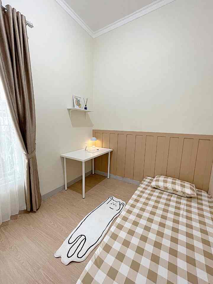 Beige and white toned compact studio room featuring a checkered bed, cat-shaped rug, and a small desk with lamp in a natural style