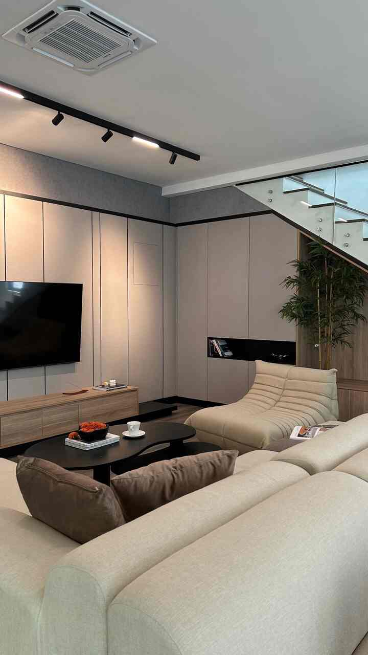 This room is a comfortable modern living room with a large cream sofa and lounge chairs. There is a black coffee table with cups and simple decorations on it. The walls use gray panels, with a television neatly installed. In the corner of the room there are ornamental plants that give a fresh impression. The ceiling is equipped with spotlights and air conditioning for comfort. The overall design is minimalist and elegant. #livingroom #modernlivingroom #ruangtamuminimalis #pohonbambu #tvsamsung #sofa #cushion #accasette #ackaset #gree #smallhome #comfyhome #comfortable #modern #minimalist #contemporary #industrial