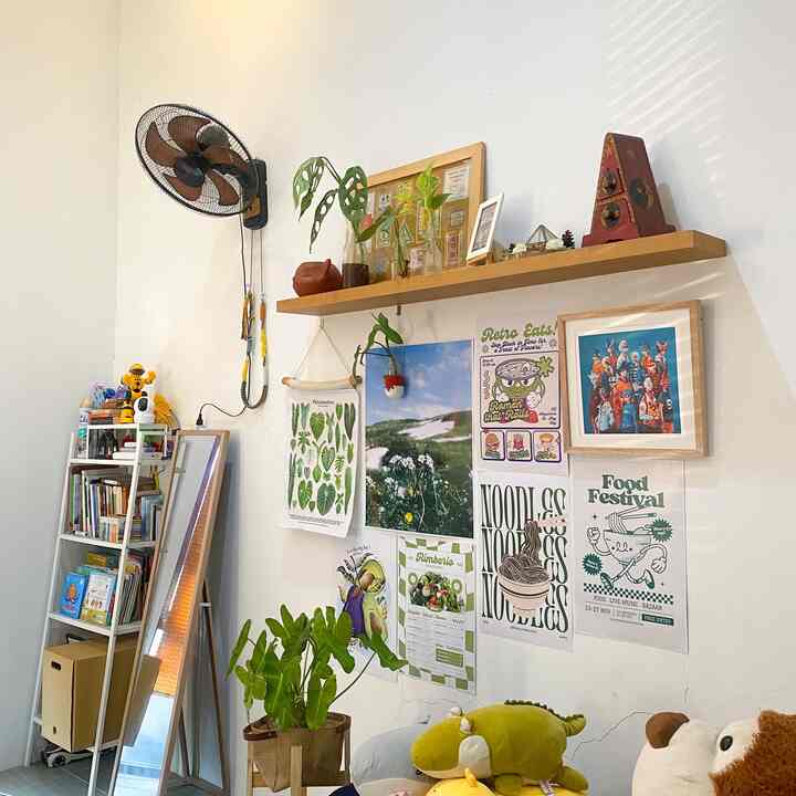 Small room with white walls and wooden shelf, decorated with colorful posters and green plants creating a cozy atmosphere