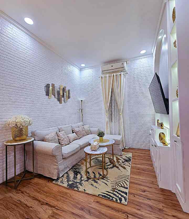 Bright living room with white brick walls and brown wood flooring, featuring beige sofa and carpet in a clean, modern setting