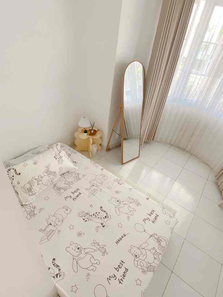 Bright white and natural toned bedroom featuring a single bed, oval standing mirror, beige curtains, and simple table lamp in a clean space