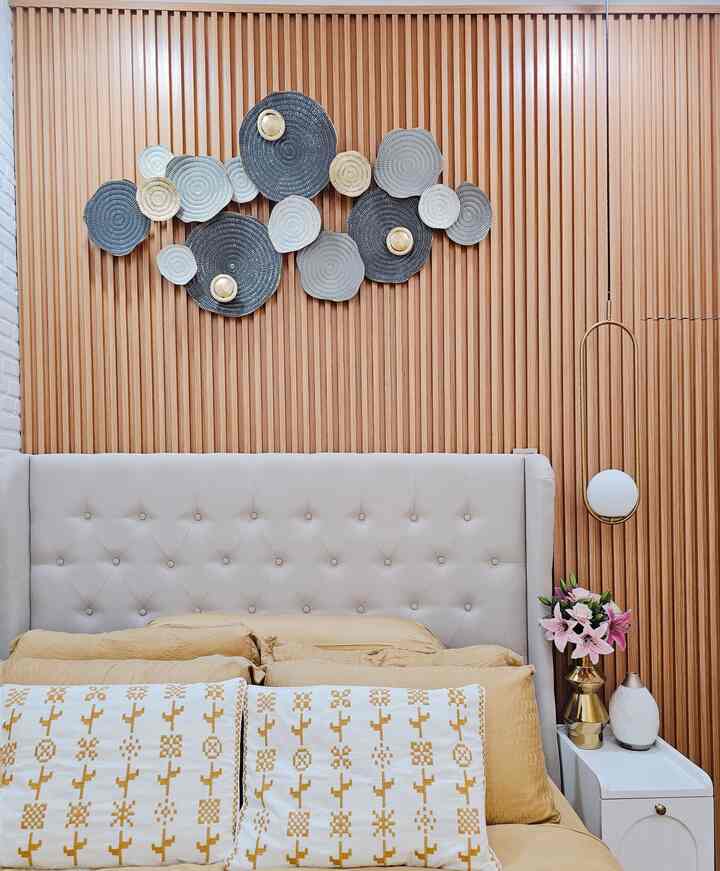 Beige and wood tone bedroom featuring a tufted bed with cushions and bedding, accented by a gold pendant light creating an elegant atmosphere