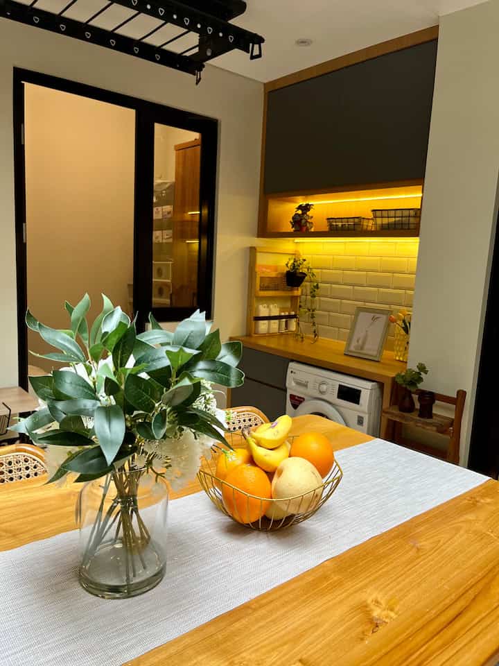 Wood tone and white kitchen dining area featuring a table with a plant vase and gold fruit basket, creating a warm atmosphere