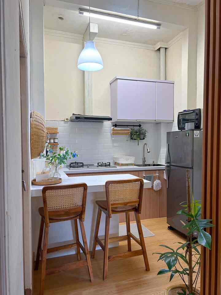 White tile walls and brown wooden furniture define a compact kitchen with a central pendant light, creating a practical and cozy atmosphere