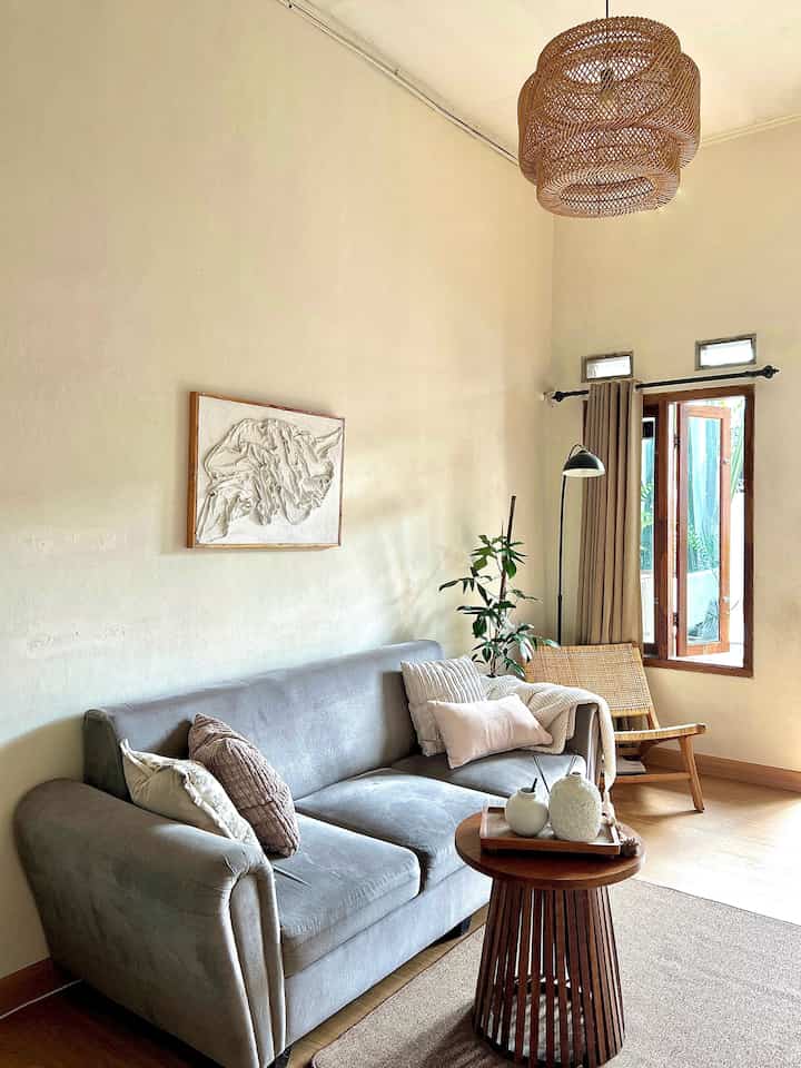 Beige and wood tone living room featuring a light gray sofa, rattan armchair, pendant light, and floor lamp creating a cozy atmosphere
