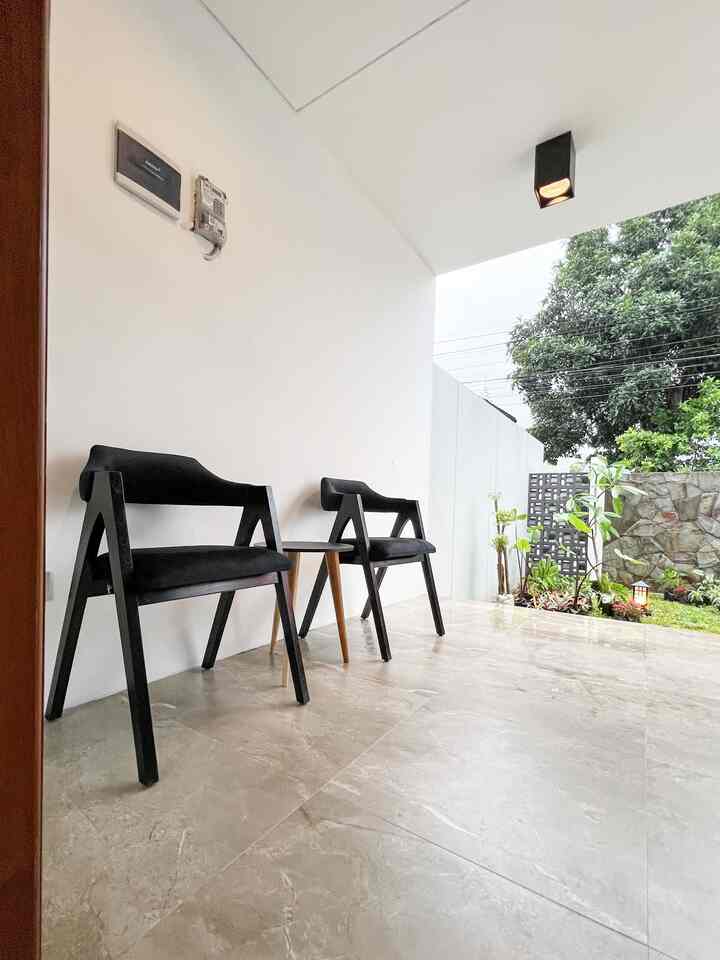 Modern balcony space featuring two black armchairs against white walls and natural tone flooring with an open garden view