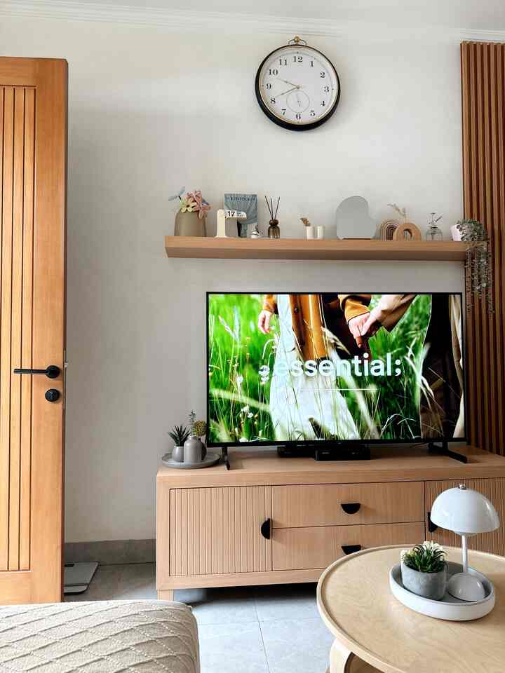 Bright white walls with wood tone furniture, TV stand and wall clock in a neat living room space