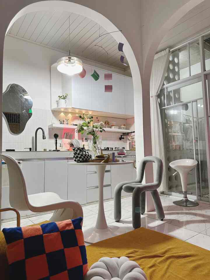 Modern living room and kitchen space in white and yellow tones, featuring unique chairs and round table with a simple interior design