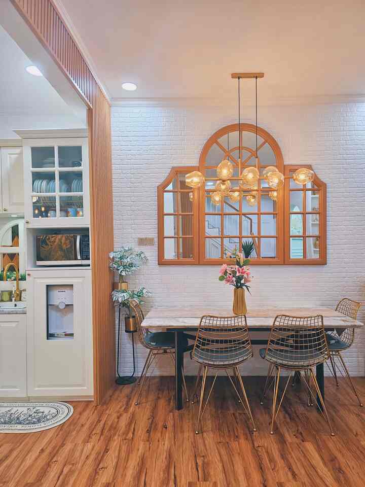Bright dining room with white brick walls, natural wood flooring, and gold accents in lighting and chairs