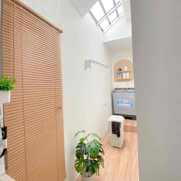 Bright, narrow laundry space with white walls, wood tone floor, beige blinds, and green plant accents creating a practical atmosphere