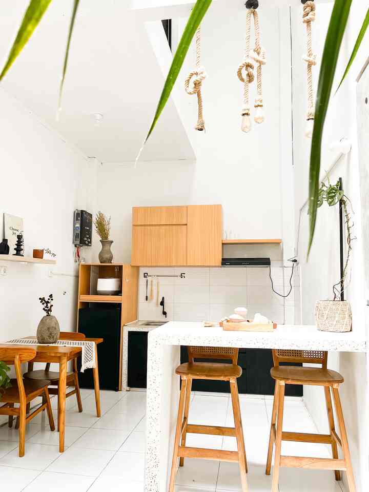 A compact kitchen and dining room in white and brown tones featuring wooden furniture and bar stools with a clean atmosphere