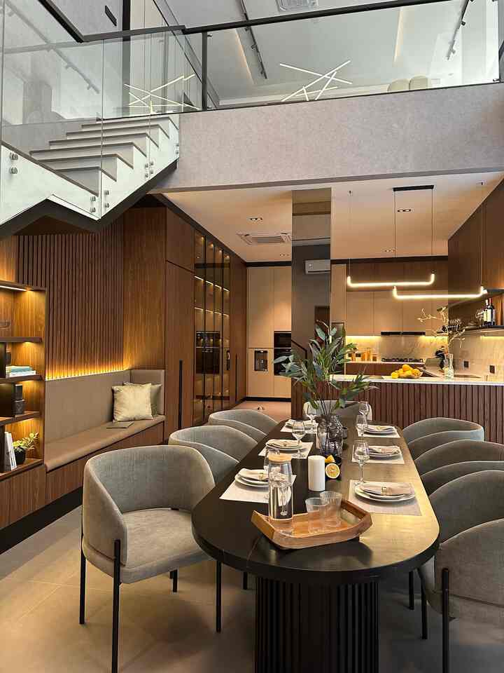 Ruangan ini merupakan contoh desain open space yang elegan dan modern, memadukan area dapur dan ruang makan secara seamless tanpa sekat. Konsep ini memberikan kesan luas, terang, dan nyaman, cocok untuk hunian masa kini yang mengutamakan efisiensi ruang.
	1.	Desain Dapur
Bagian dapur memiliki kabinet bergaya minimalis dengan warna netral seperti krem dan kayu cokelat gelap, menciptakan nuansa hangat sekaligus modern. Sentuhan backsplash marmer menambahkan kesan mewah, sementara pencahayaan tersembunyi di kabinet atas memberi suasana hangat dan fungsional.
	2.	Ruang Makan
Area makan dilengkapi meja panjang dengan desain kaki melingkar berwarna hitam, dipadukan dengan kursi berlapis kain abu-abu yang empuk. Penataan ini menampilkan kesan formal namun tetap nyaman untuk berkumpul bersama keluarga atau teman.
	3.	Pencahayaan
Lampu gantung modern dengan bentuk unik menjadi pusat perhatian sekaligus memperkuat estetika ruangan. Sinar lampu kuning hangat membuat suasana lebih intim dan welcoming.
	4.	Keseluruhan Konsep Open Space
Penggabungan kedua area ini tanpa dinding pembatas menciptakan aliran ruang yang lancar dan mempermudah interaksi antar penghuni. Kehadiran elemen dekoratif seperti tanaman dan elemen kayu menambah sentuhan natural di tengah desain modern.

Ruangan ini sangat cocok untuk generasi muda yang menyukai desain minimalis, fungsional, dan tetap estetis.
#kitchen #livingroom
#kitchenset #hplaica #ovenbosch #microwavebosch #lilinikea #mejamakan #dapuropenspace #rumahtanpasekat