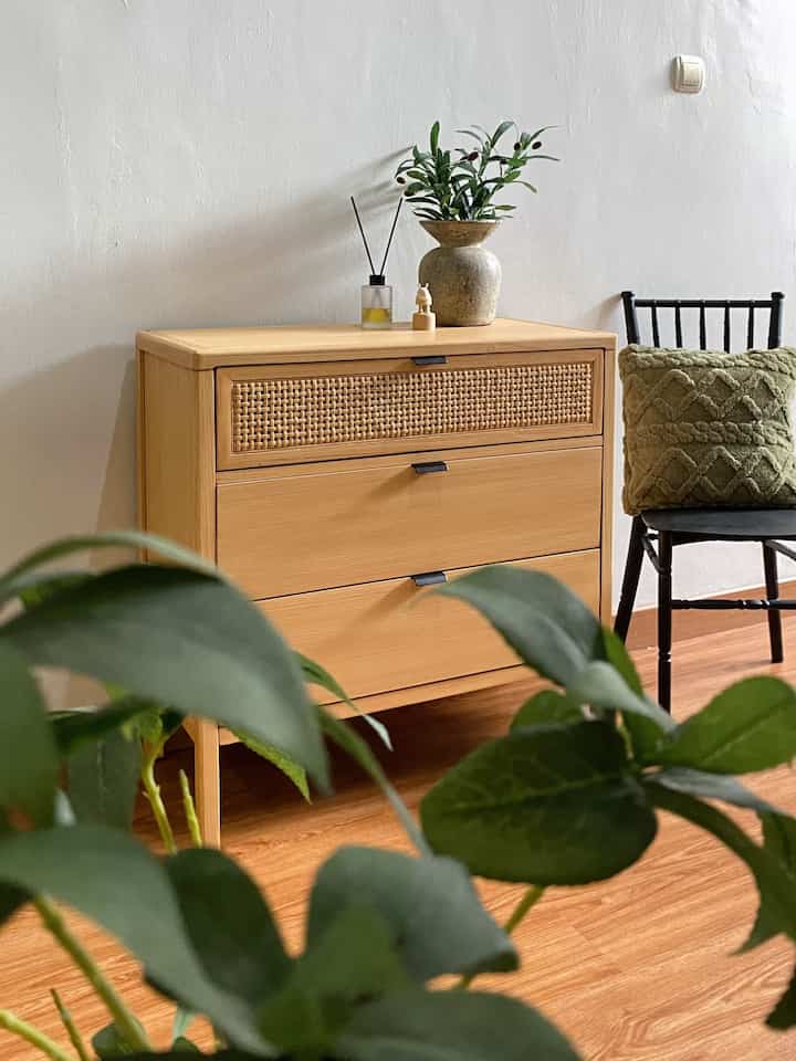 Natural tone beige entrance area featuring a wooden chest of drawers and a black chair with green cushion in a cozy setting