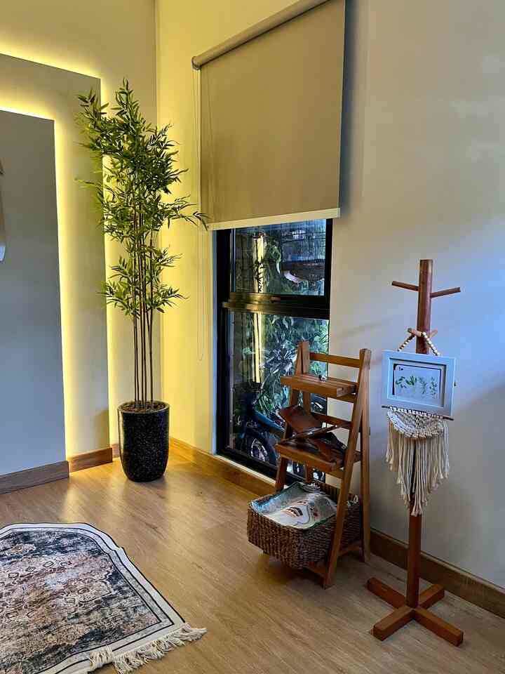Beige tone walls and wood-tone flooring feature plant and wooden furniture in a cozy corner space