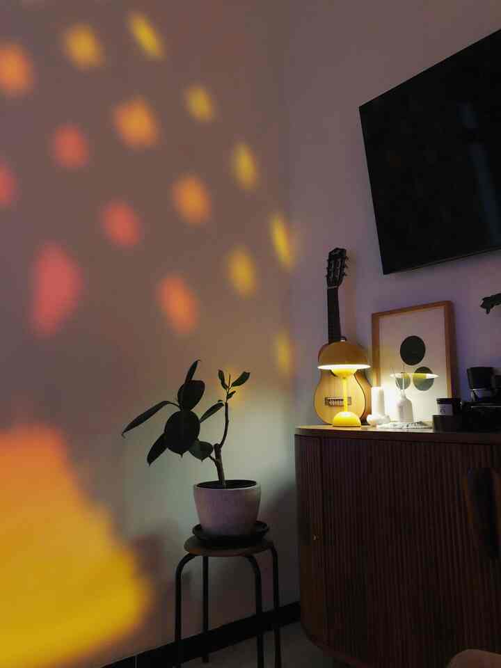 Compact living room corner with yellow lighting and brown furniture featuring a guitar and a plant, creating a cozy atmosphere