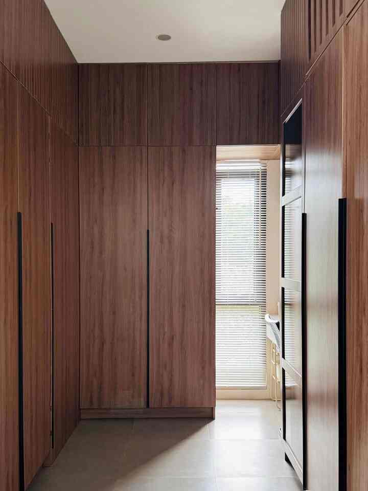 Wood tone built-in closets filling a narrow entrance space with blinds on the window allowing natural light, showcasing a modern interior design