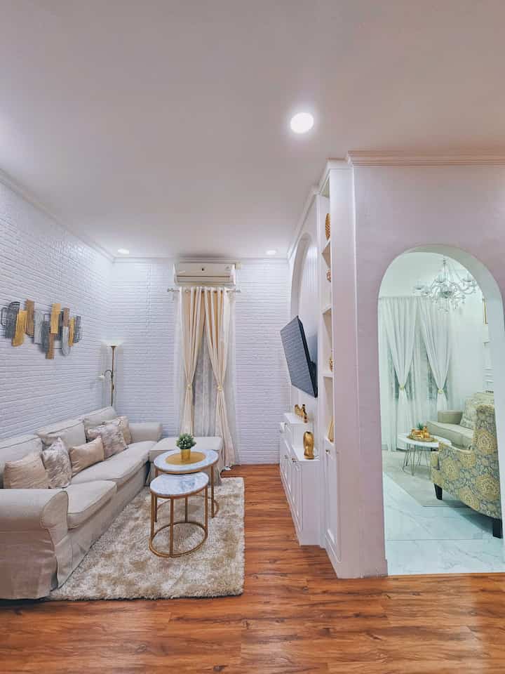 Bright white and brown toned small living room featuring a beige sofa and round coffee tables with a warm, cozy atmosphere