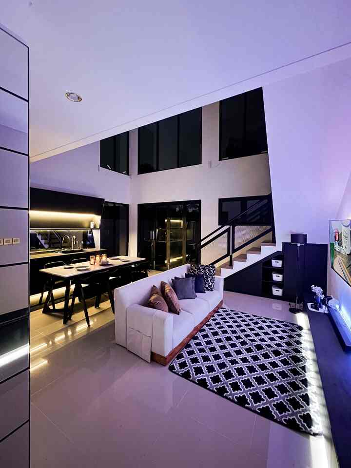 Modern living and dining room in black and white tones featuring a white sofa, staircase, and a patterned carpet in an open layout