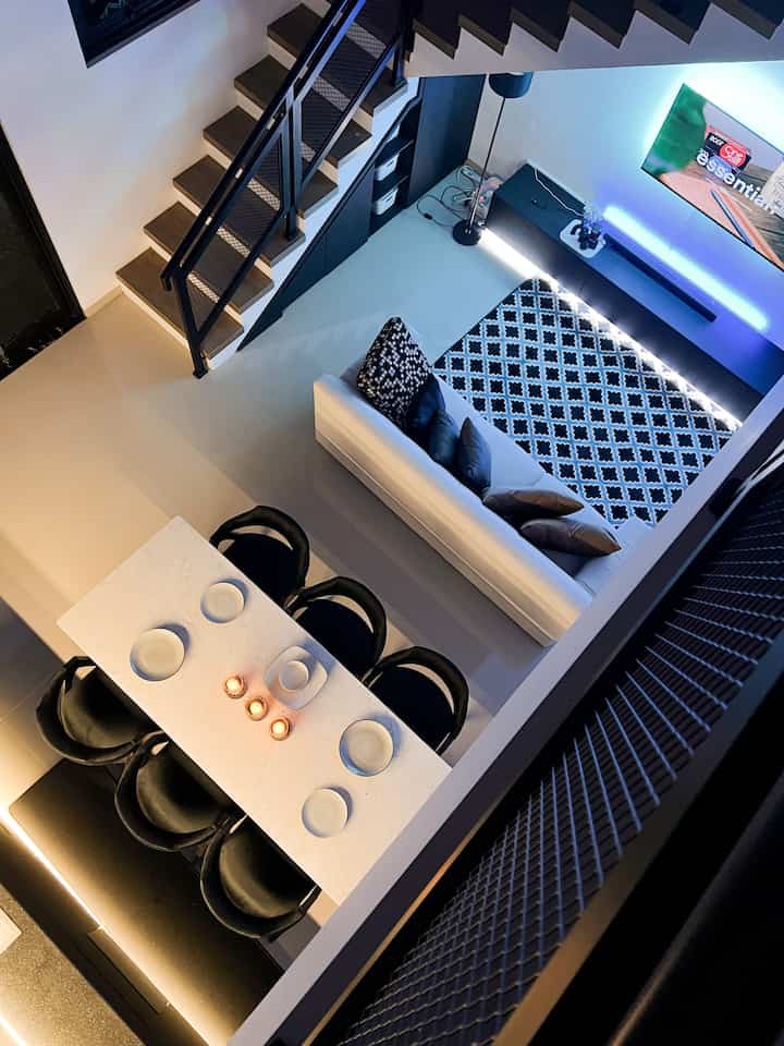 Modern living and kitchen space in white and black tones featuring sofa and dining table with cozy nighttime ambiance