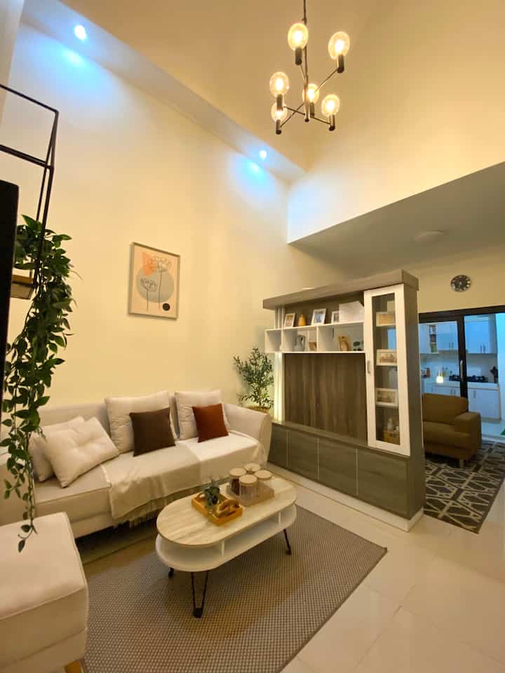 Warm beige and white toned living room featuring sofa, coffee table, and pendant lighting with cozy ambiance