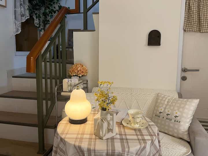 Beige and white-toned living room featuring a round table with a table lamp and vase, accompanied by a sofa in a simple natural setting