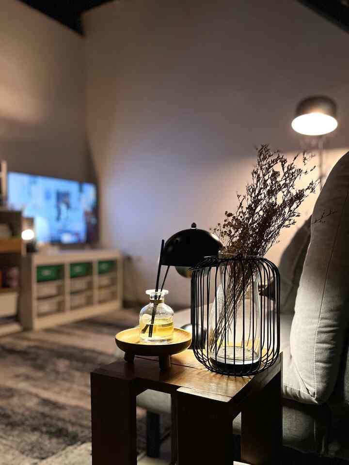 Warmly lit living room with natural brown and black furniture tones, a wooden side table next to the sofa holding diffuser and lamps