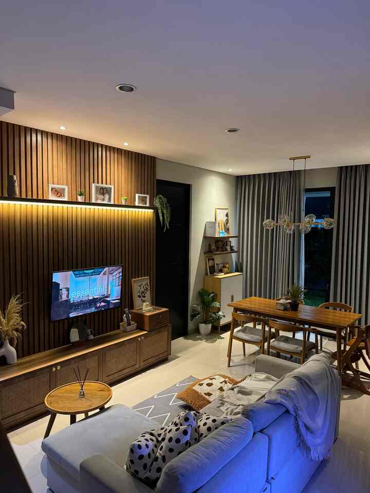 Modern natural living and dining room at night with gray sofa, wooden furniture, and warm lighting