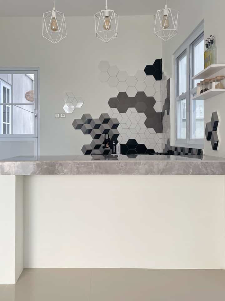 Monotone modern kitchen space featuring hexagonal mosaic tile wall and simple pendant lights with a clean design